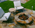 Raised fire ring entertainment area designed in backyard oasis with swimming pool installation in the background.