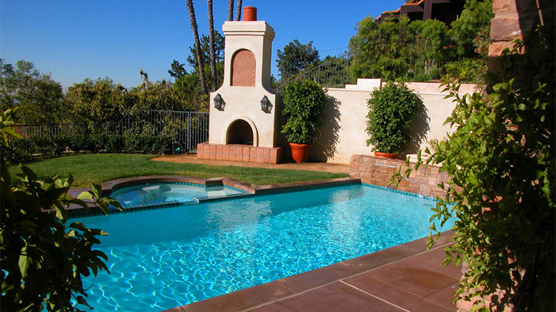 In this dramatic entertainment space, a towering fireplace overlooks an attached spa and pool. Classically simple, geometric shapes are warmed by the earth tones of stucco, tile and brick. In the evening, the effect is magical.