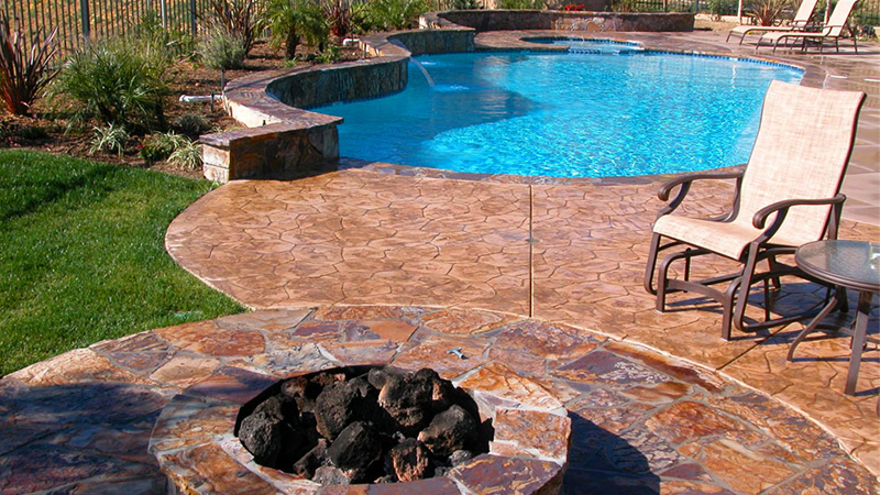 In this Tustin home, guests can wander between the warmth of a fire ring and the cool pleasures of a spa and pool, walking across a stone deck to concrete surfaces with stamped and natural, brushed textures. Organic architectural shapes are complemented by a casual Swan Pools landscape design.